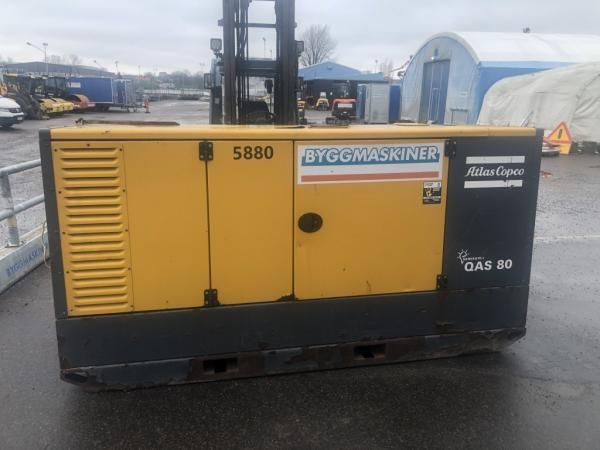Gulsvart Atlas Copco QAS 80 byggmaskin på en byggarbetsplats.